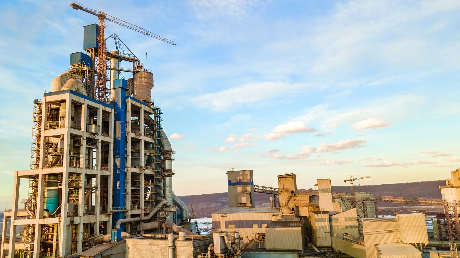 Cement plant with a tall kiln tower, silos and cranes under a blue sky