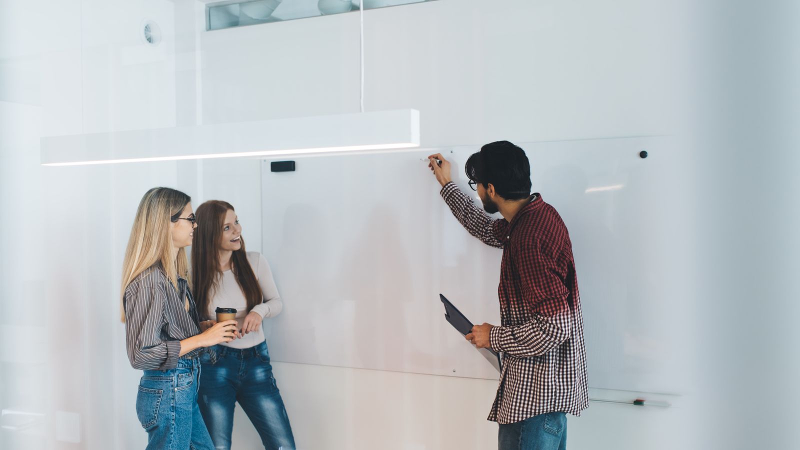 Man writing on a whiteboard while two colleagues watch