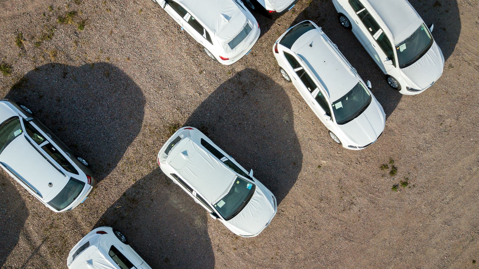 Aerial view of new white cars with protective covers parked on gravel