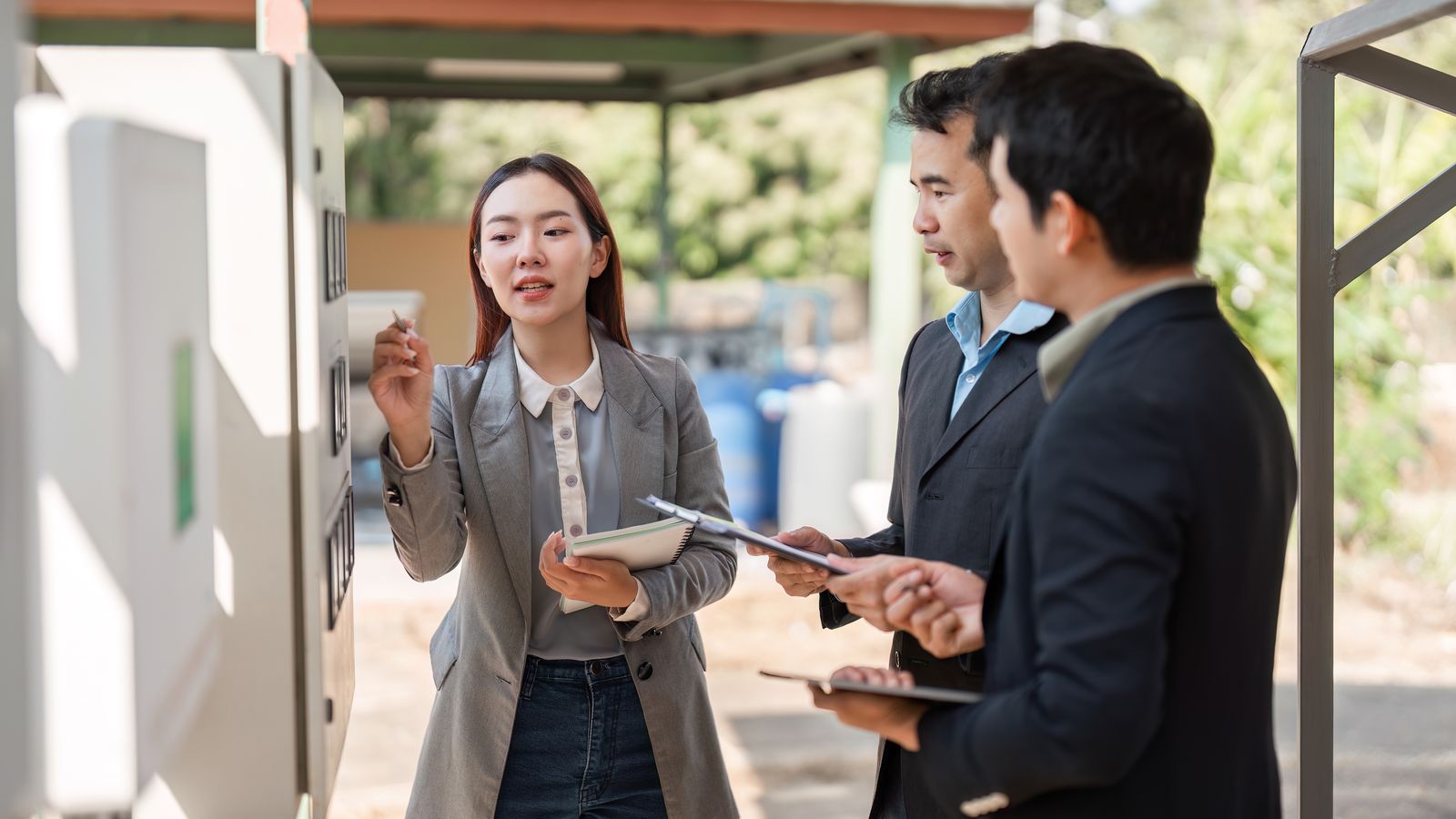 Three business people with notebooks beside an outdoor electrical cabinet