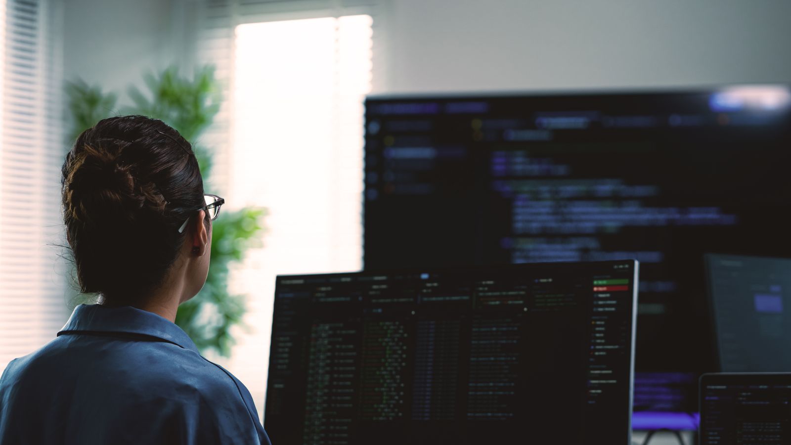 Woman in glasses looking at screens showing code
