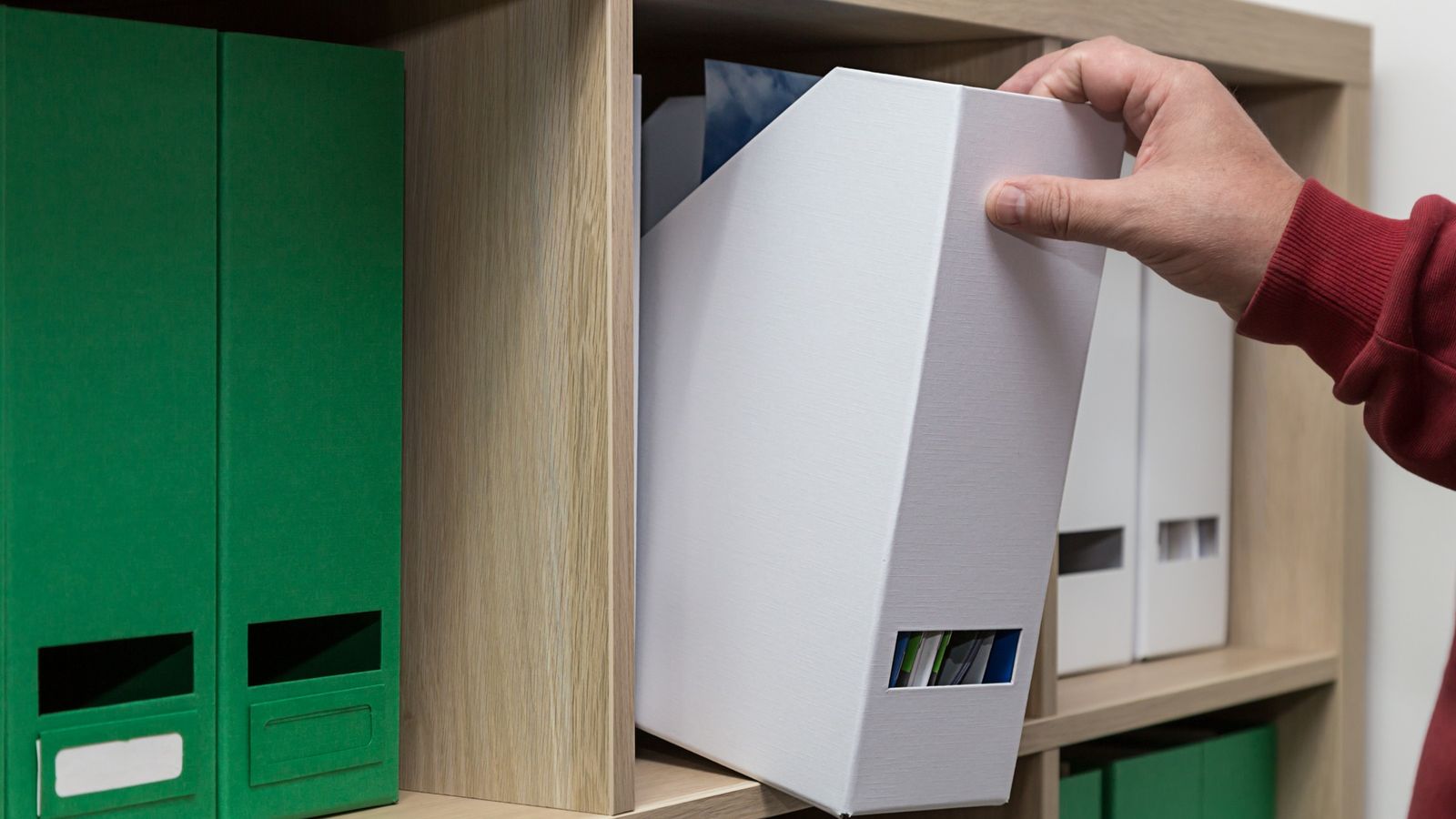 Hand filing a white box folder onto an office shelf