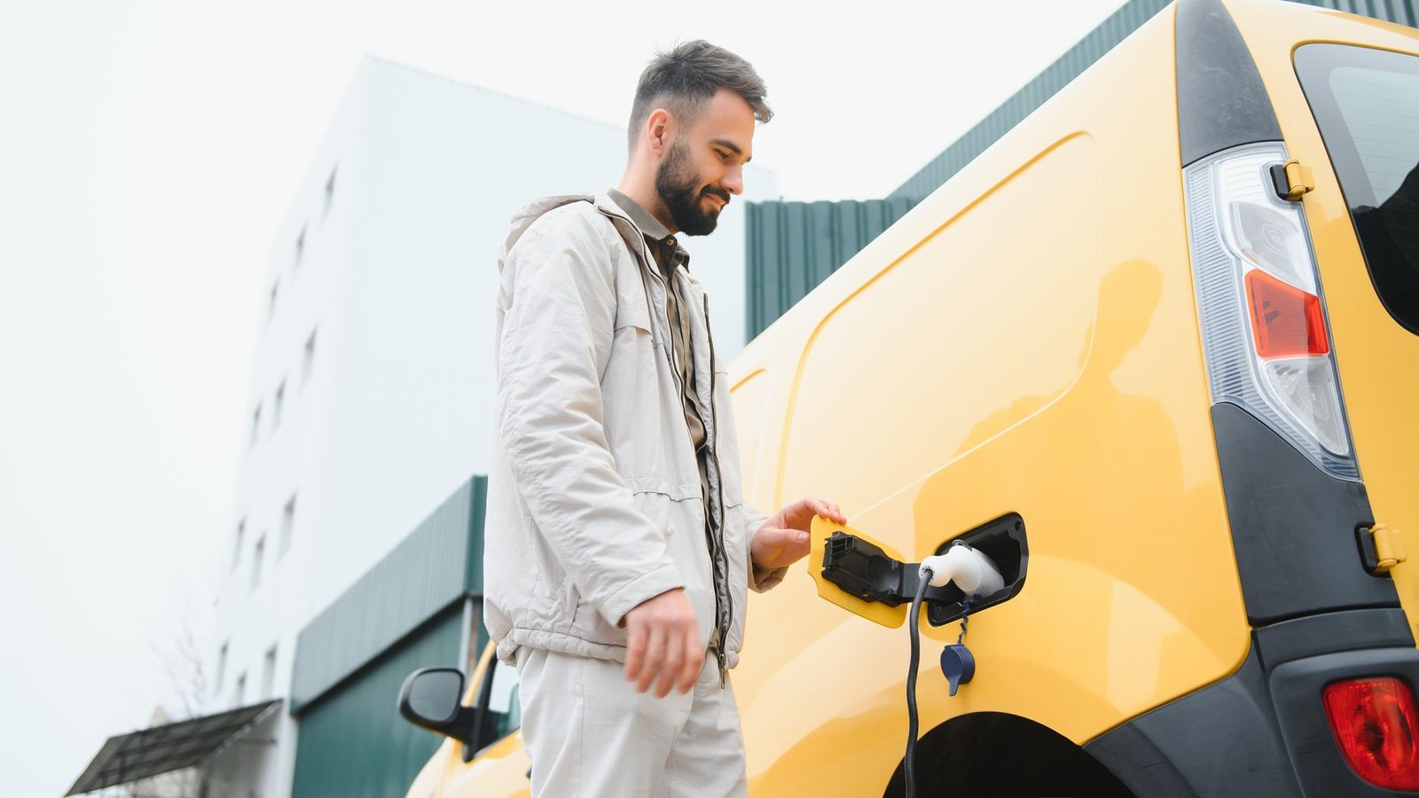 Man plugging a charging cable into a yellow electric van