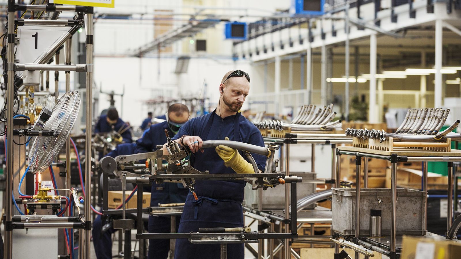 Workers in overalls assembling bent metal tubes at workstations on a factory production line
