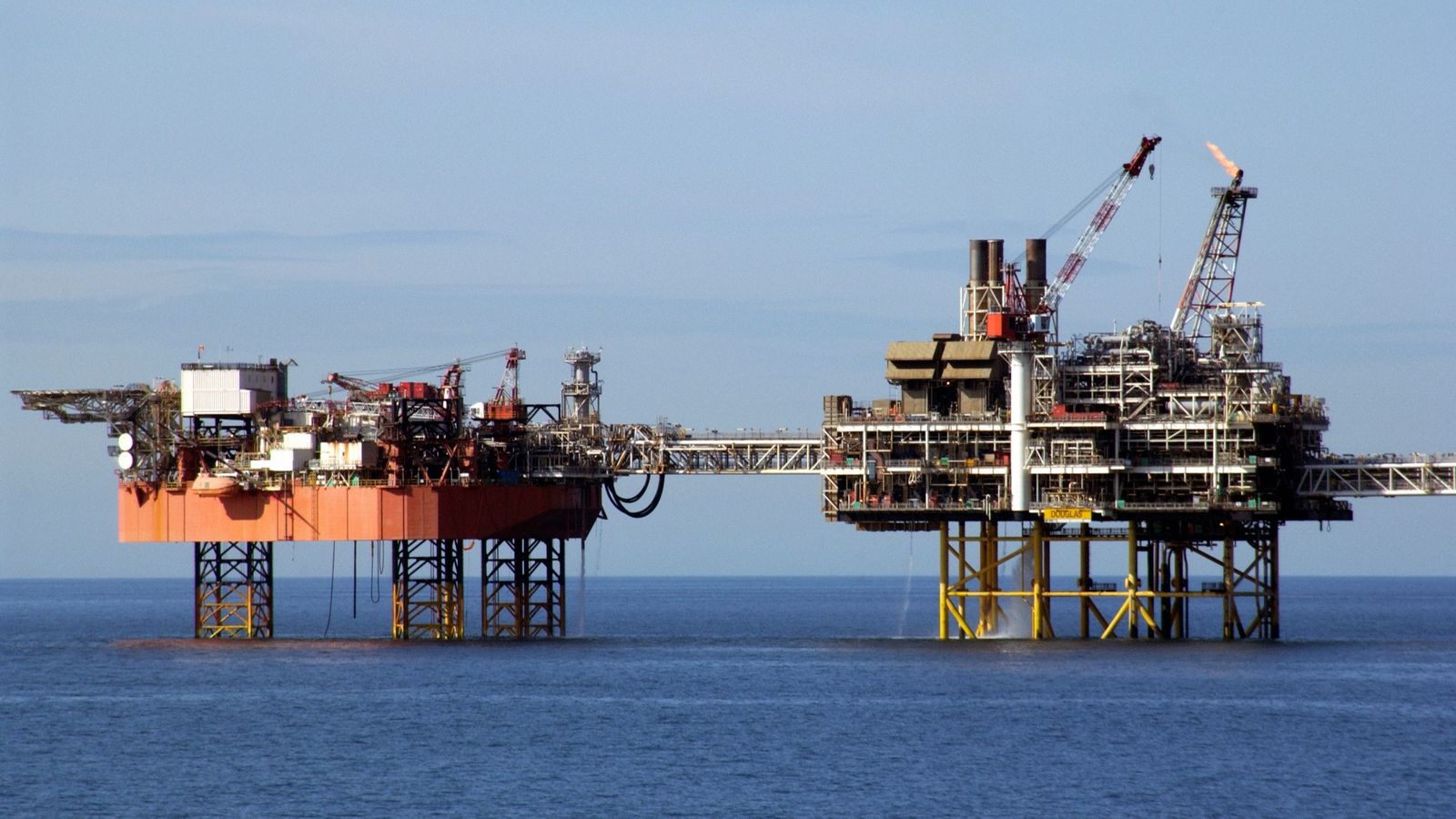 Two linked offshore oil and gas platforms in calm open sea, one burning a gas flare