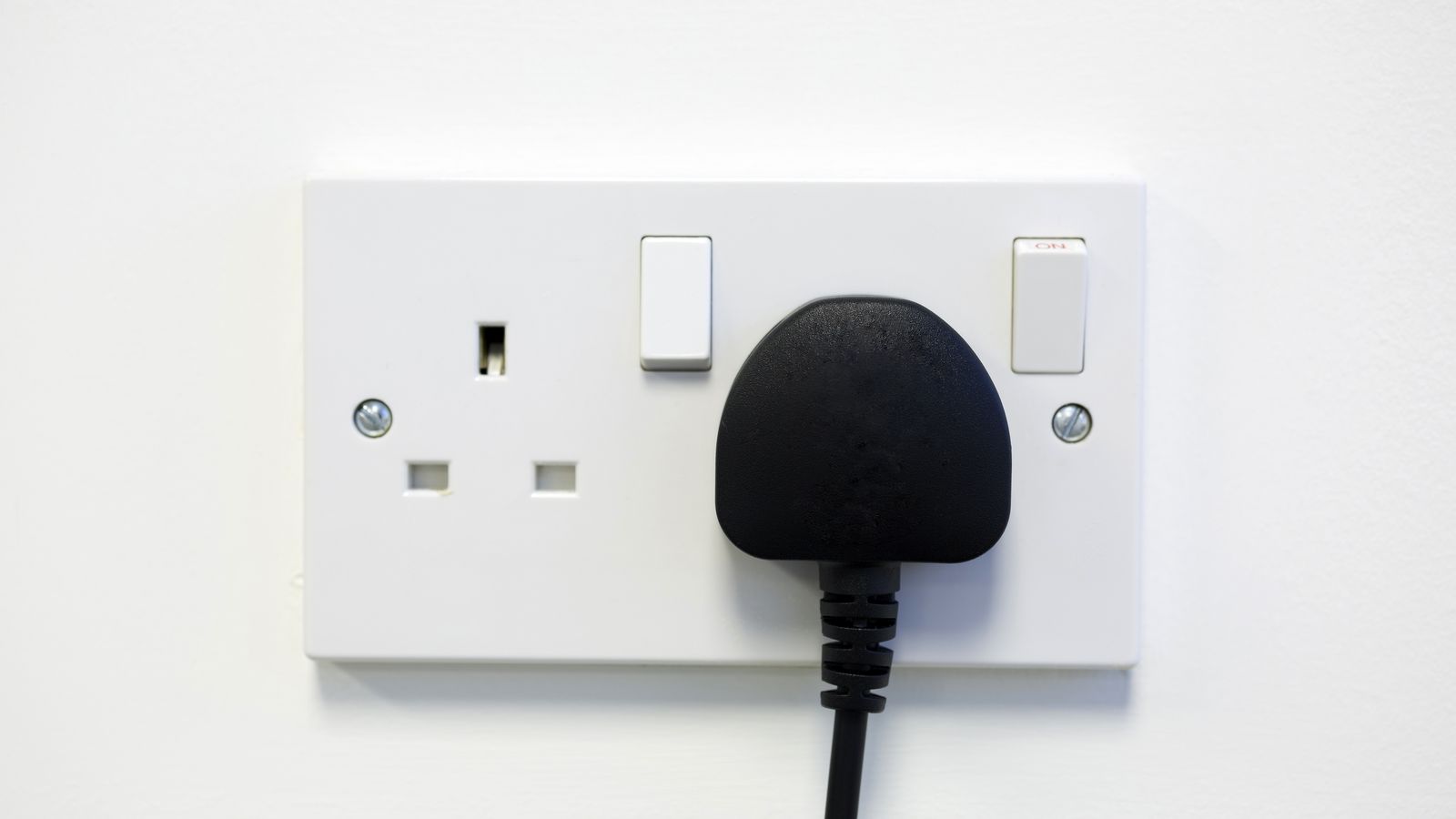 Black plug in a white UK three-pin wall socket