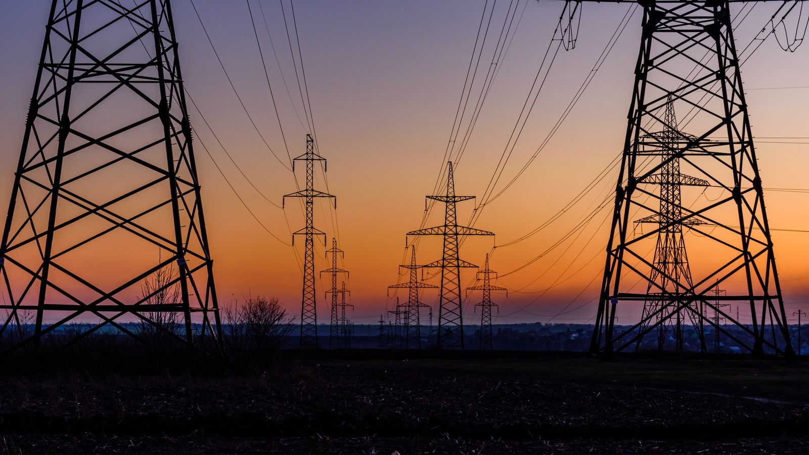 Silhouetted electricity pylons and power lines across a rural field at sunset