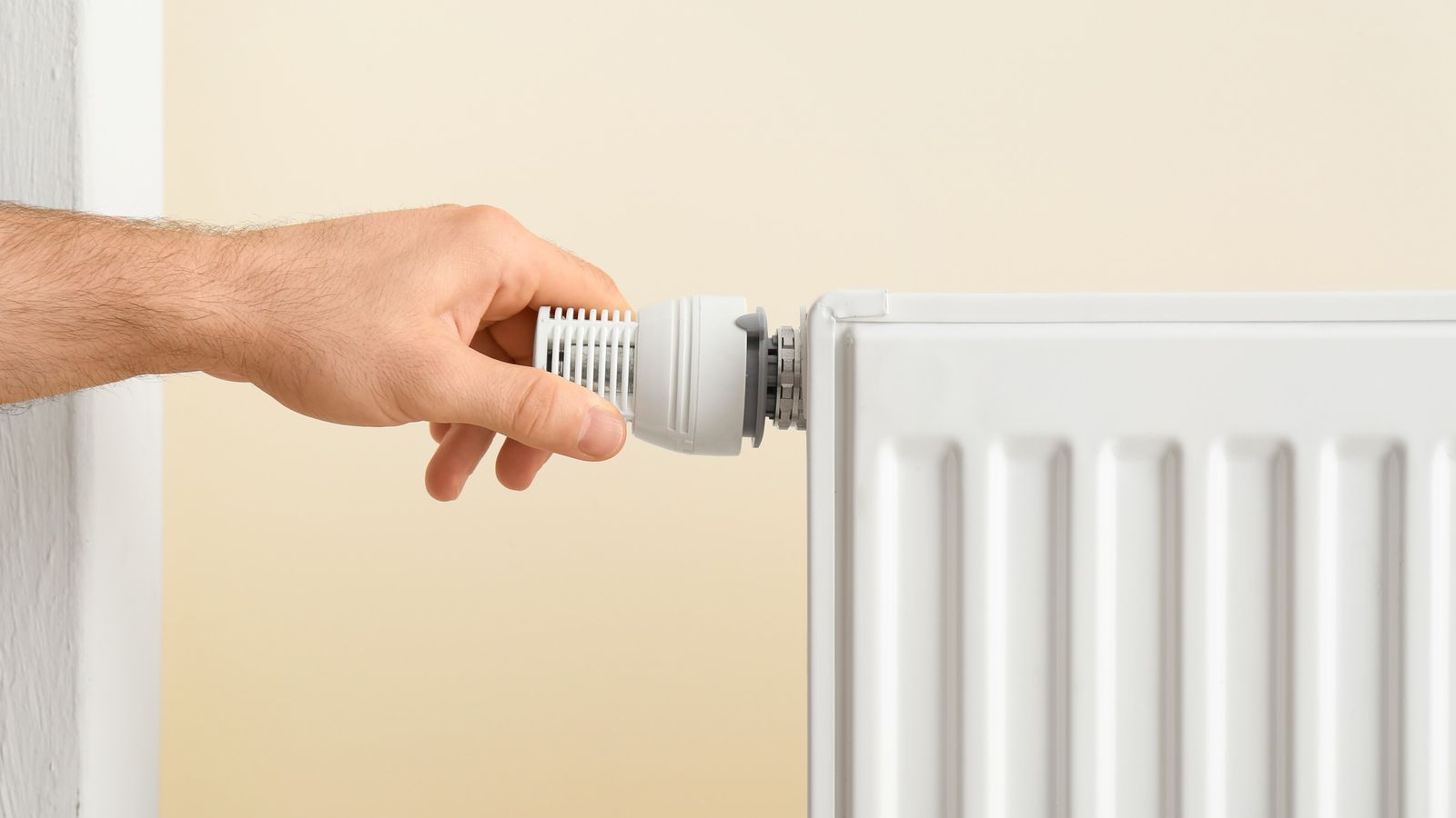 Hand turning a thermostatic valve on a white panel radiator