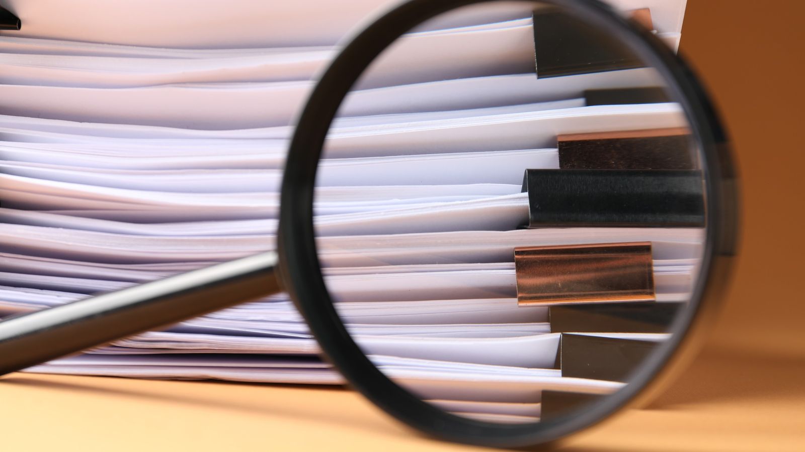 Magnifying glass held over a stack of paper documents and files