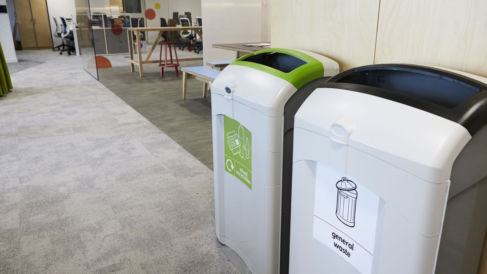 Mixed recycling bin with a green lid next to a general waste bin in an open-plan office