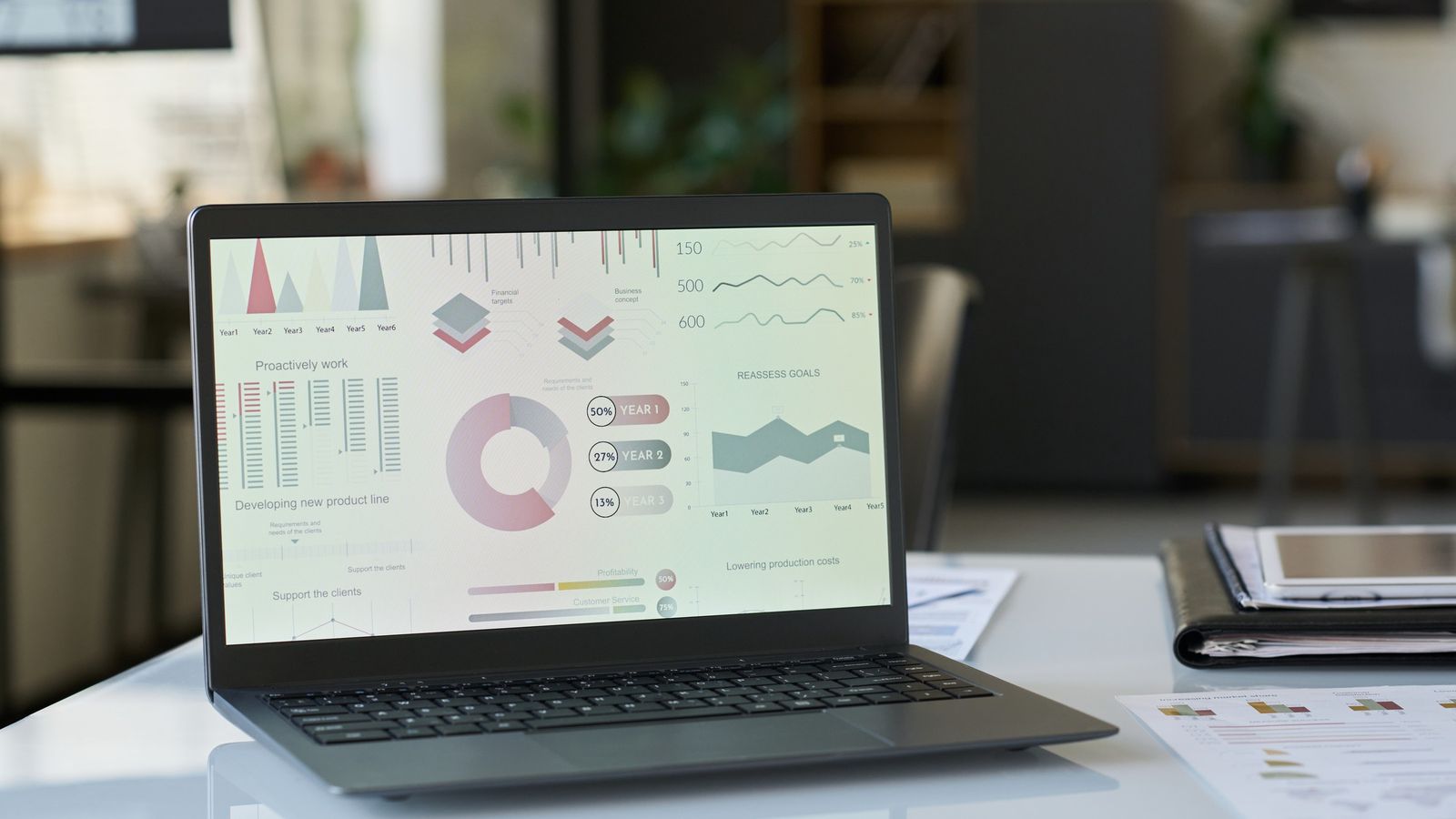 Laptop showing charts and graphs on a desk beside printed papers