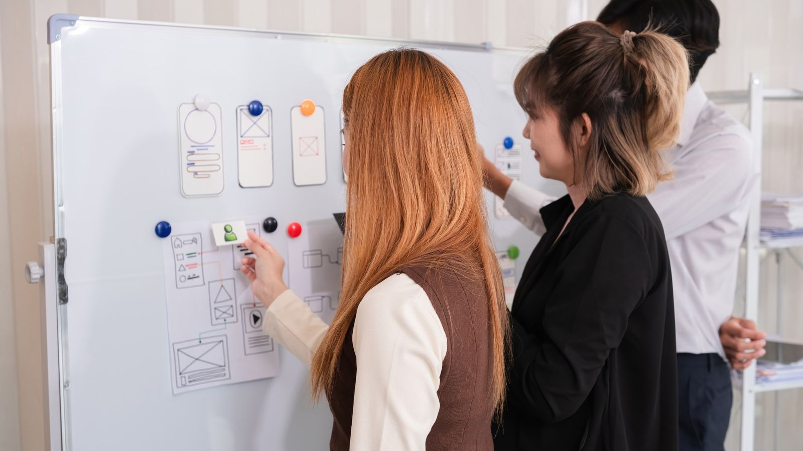 Colleagues planning with notes and magnets on an office whiteboard