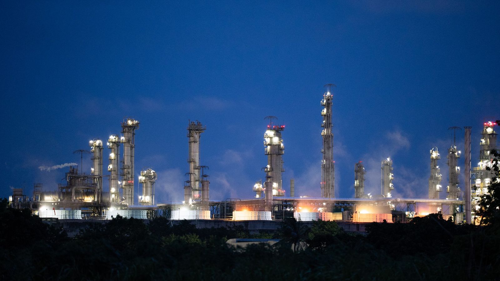Refinery towers and stacks lit up against a deep blue dusk sky