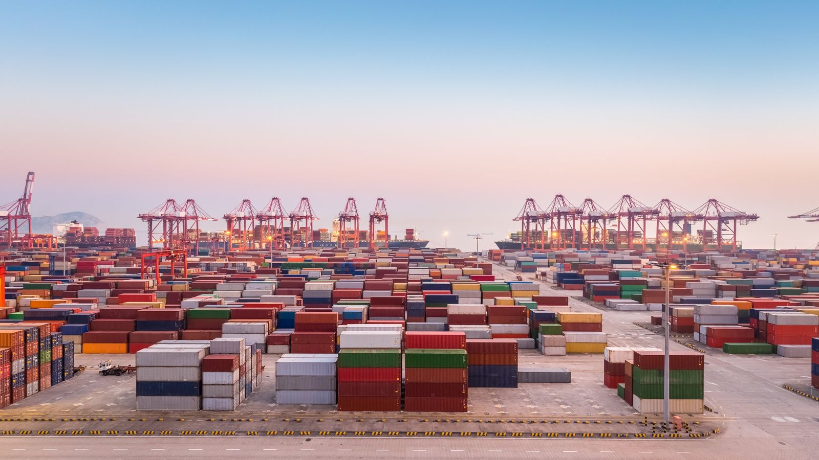 Container terminal with stacked containers and distant gantry cranes at dusk