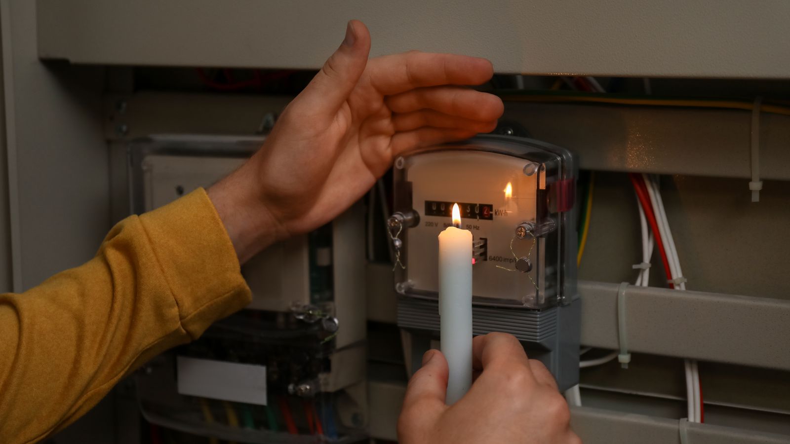 Hand holding a lit candle beside an electricity meter during a power cut