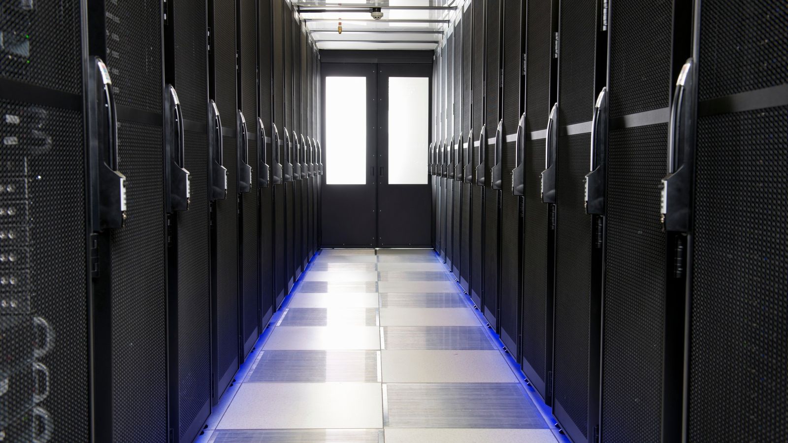 Long data centre corridor between rows of black server racks
