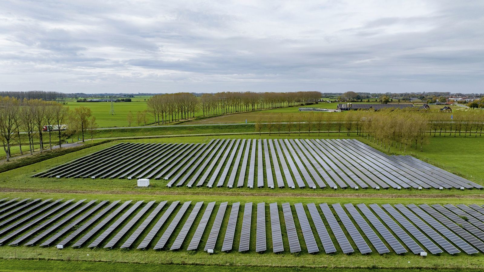 Rows of ground-mounted solar panels in a green field under a cloudy sky