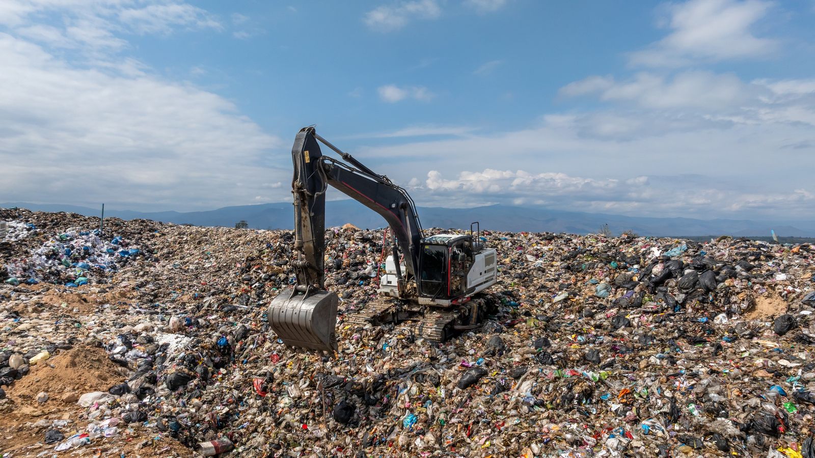 Excavator working on top of a landfill heap under a blue sky